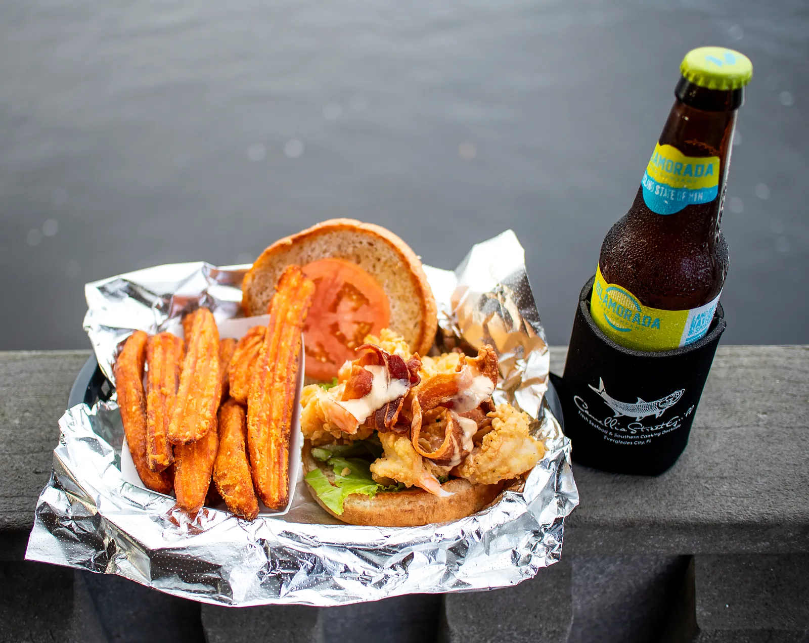 A sandwich basket with sweet potato fries and a beer