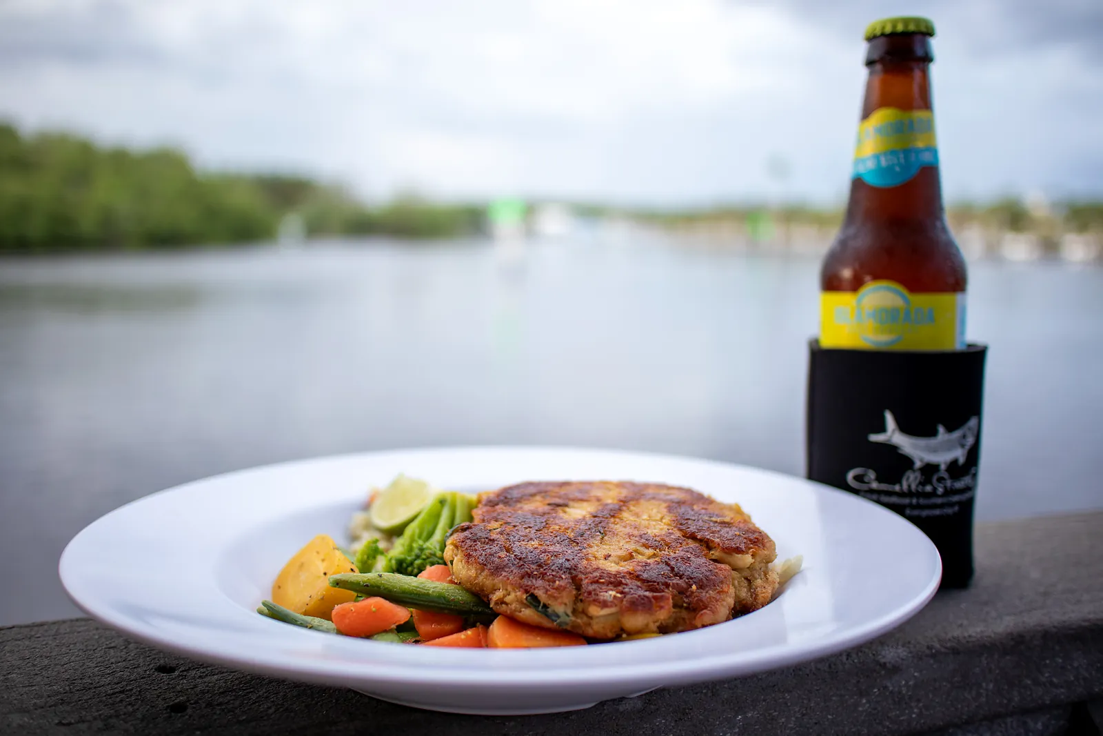 A plate of seafood with a cold beer on the rail, river behind